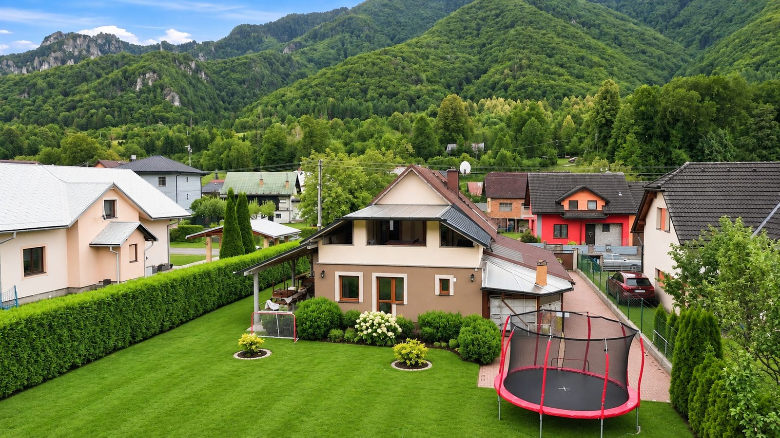 Chata Ranto from above, with the garden, trampoline and goal, and forested ridges with rocks behind the house